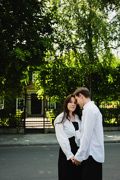 Young married couple stands close together outdoors, sharing a loving gaze amidst vibrant green foliage and soft sunlight