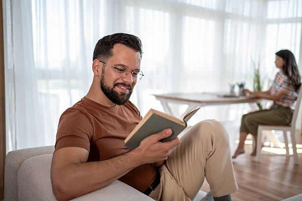 istock Young man reading a book while woman works on laptop 2229066944