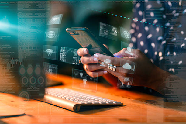 An individual uses a smartphone and keyboard, surrounded by a holographic interface with technology icons, symbolizing innovation, connectivity, and user interaction in digital environments.