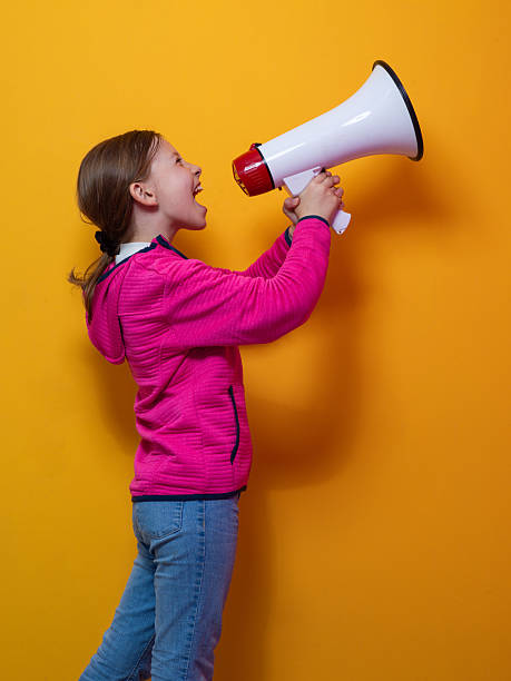 istock Excited girl shouting into megaphone against orange background 2229070136