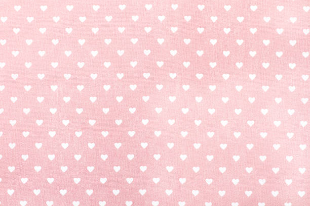 A pink fabric with white hearts in a close up view