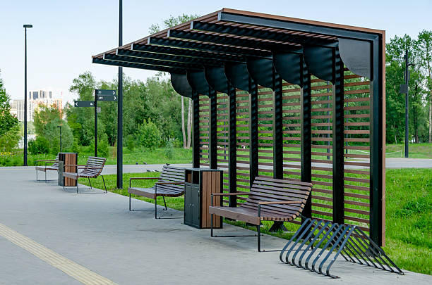 Empty recreation area in a park featuring modern wooden benches and bike racks under a shaded structure. Lush greenery surrounds the setting, offering a peaceful retreat.
