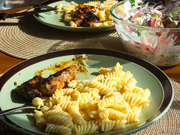 Grilled chicken and rotini pasta are being enjoyed for lunch, with a side of fresh cucumber and tomato salad, creating a healthy and satisfying meal