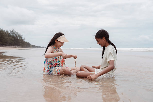 istock Multicultural and Asian daughters sitting together on the beach, smiling and enjoying a peaceful moment of friendship, childhood joy, diversity, and seaside happiness. 2229074793