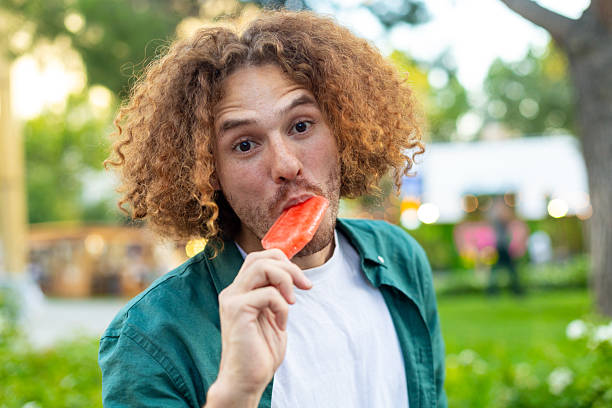 istock Young man enjoying a refreshing popsicle in a park 2229076063