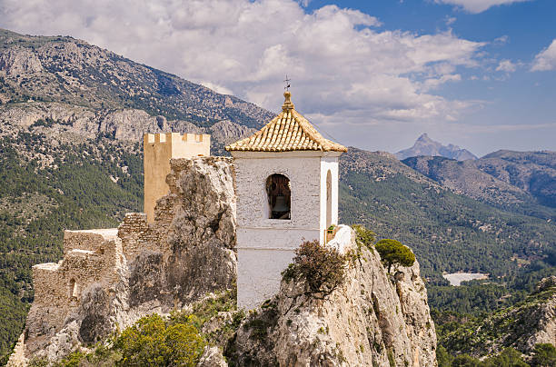 Cocentaina, Alicante, Valencia, Spain - November 8, 2025: Cocentaina castle tower proudly standing on a rugged cliff under a vibrant blue sky with scattered clouds, showcasing a historic landmark in the Valencian Community for tourism and travel