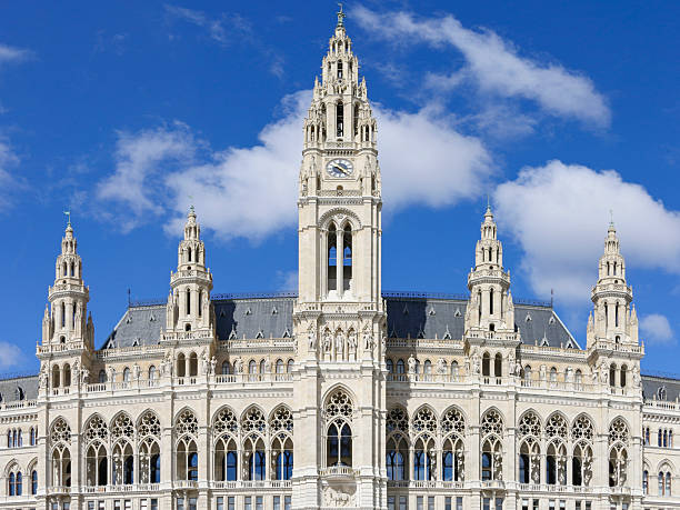 Front view of Vienna City Hall (Rathaus) in Austria, showcasing its Neo-Gothic architecture and central clock tower against a blue sky with clouds.
