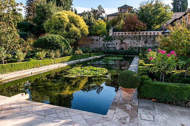 Alhambra complex in Granada town, Andalusia, Spain. Serene garden with a pond, lush greenery, and vibrant flowers.