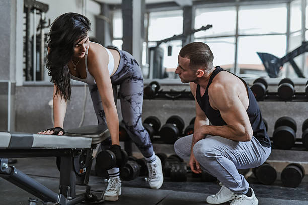 istock Woman Exercising One Arm Dumbbell Back Row As Instructor Is Observing Closely 2229080415