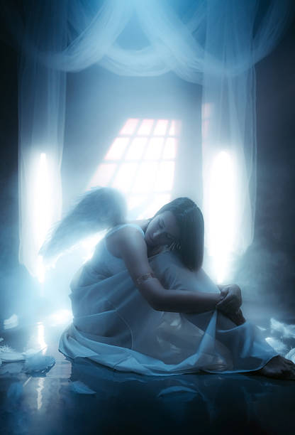 istock Angel Sitting On The Floor While White Light Is Shining Behind Her 2229082034