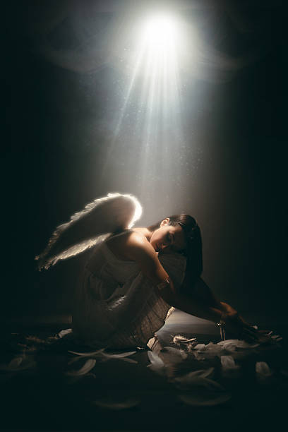 istock Angel Sitting On The Floor While White Light Is Shining Above Her 2229082164