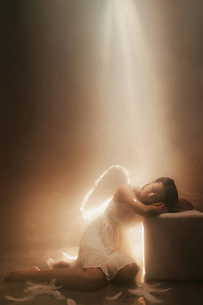 istock Angel Sitting On The Floor While White Light Is Shining Above Her 2229082448