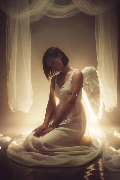 istock Angel Sitting On The Floor While White Light Is Shining Behind Her 2229083195