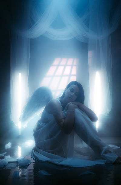 istock Angel Sitting On The Floor While White Light Is Shining Behind Her 2229083343