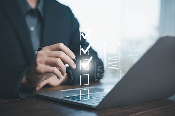 istock Business checklist and document verification concept. A businessman using stylus on virtual screen to check tasks on laptop. Digital task management, workflow process, and online form approval system. 2229084721