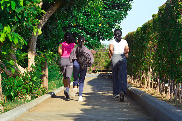 Back view of a person walking on a paved park path in sportswear and running shoes. Active lifestyle concept suitable for fitness, wellness, urban park activities, and healthy habits themes. Ideal for articles, blogs, ads, and social media campaigns about daily exercise, outdoor training, walking workouts, and weekend recreation in the city environment.