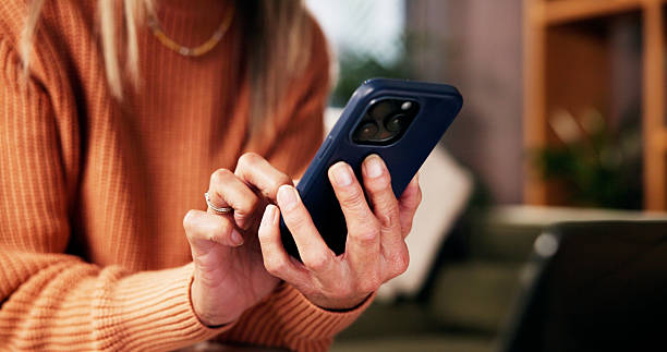 istock Hands, phone and scroll on sofa in living room with notification, contact or texting on web in retirement home. Person, relax and smartphone for chat, mobile app and social media in lounge at house 2229085397