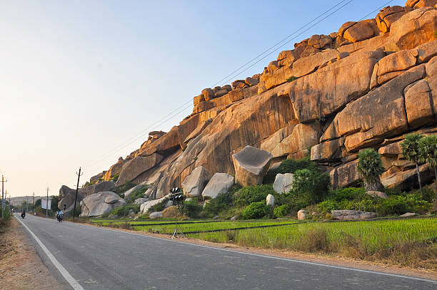 An asphalt road along a mountain with large boulders in India.