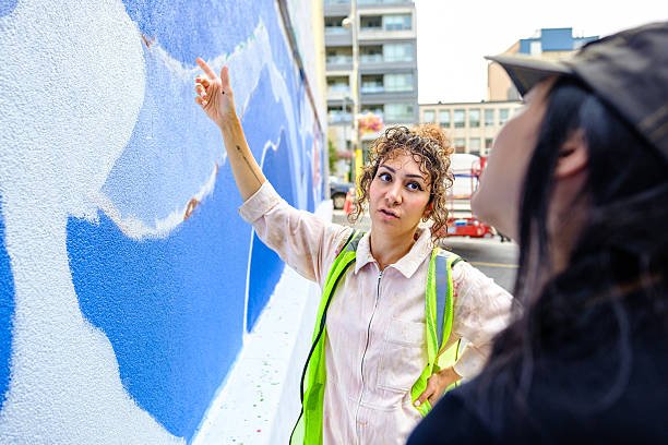 Two  women artists getting ready to paint large mural on  public building wall.  Both dressed in casual work clothes. Exterior of urban cityscape of Toronto, Ontario in Canada.