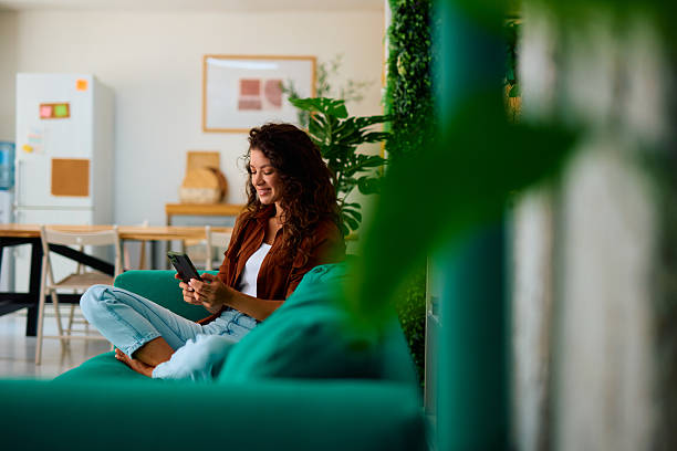 istock Young woman using smartphone sitting on sofa at home 2229088299