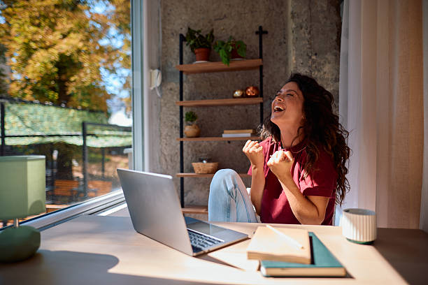 Excited young woman celebrating success while working from home office