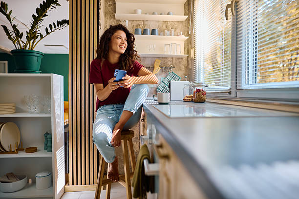 istock Young woman using phone and smiling in modern kitchen 2229088550