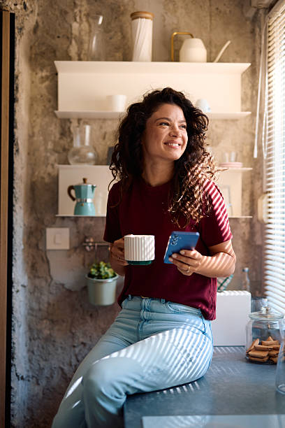 istock Young Woman Enjoying a Cup of Coffee and Using Smartphone in Kitchen 2229088598