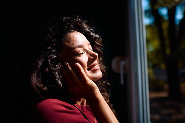 istock Young woman enjoying sunlight through window with closed eyes 2229088623