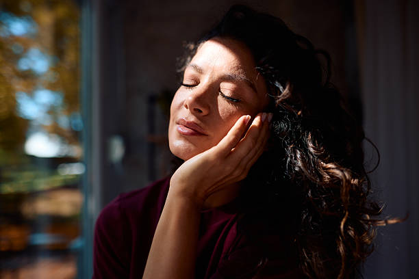 istock Serene woman enjoying sunlight through window, resting head on hand 2229088640