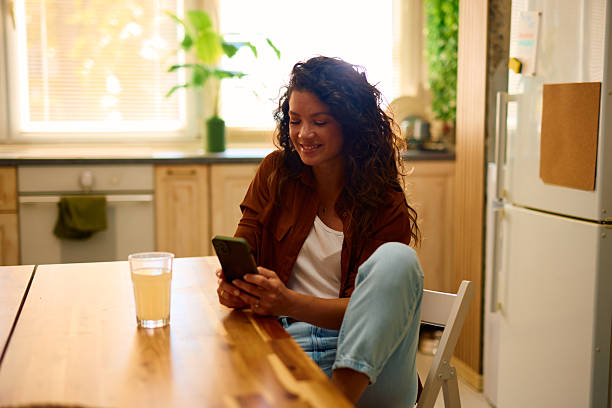 istock Young woman using mobile phone and smiling in kitchen 2229089381