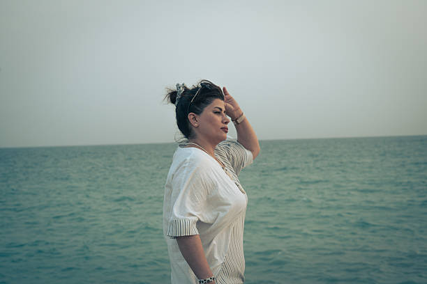 Young woman by the sea at sunset, side view with wind in hair and soft pastel sky—calm travel and lifestyle scene with copy space.