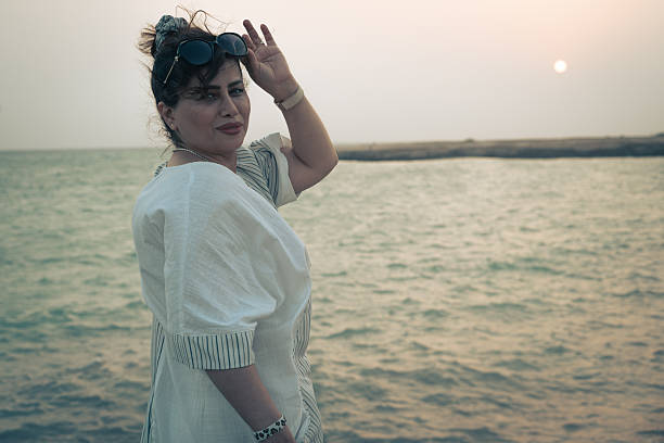 Young woman by the sea at sunset, side view with wind in hair and soft pastel sky—calm travel and lifestyle scene with copy space.