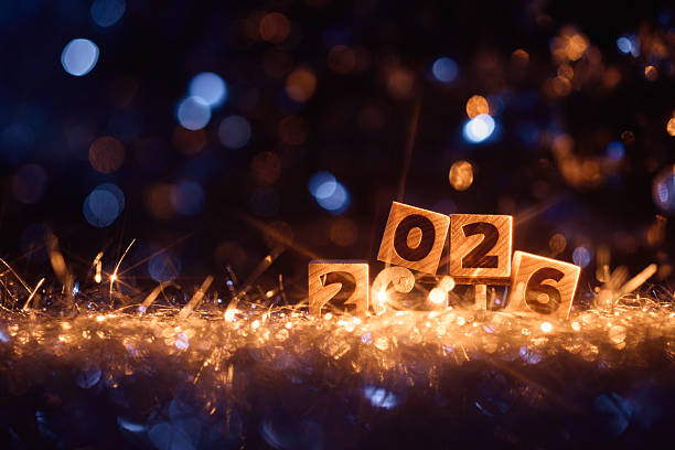 Wooden blocks forming the year 2026 sit atop a glowing bed of golden lights and festive tinsel, radiating warmth and cheer. A playful and elegant New Year image perfect for holiday promotions, invitations, and seasonal designs.