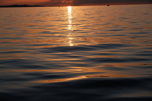 Stunning sunset over the Adriatic Sea captured from the coastline of Zadar, Croatia. The sky glows with vibrant hues of orange, pink, and purple, reflecting beautifully on the calm water. Silhouettes of ancient architecture, boats, and the famous Zadar Sea Organ add depth and character to the scenic view. Perfect for travel, nature, landscape, and European destination concepts.