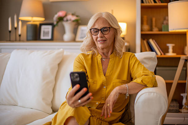 istock Senior woman relaxing on sofa using smartphone at home 2229116436