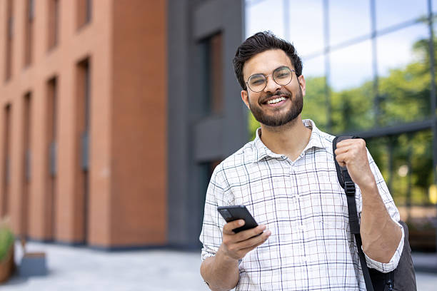 istock A smiling man holds a phone in front of a modern building. 2229123631
