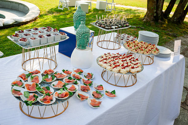 A beautifully arranged table features an array of appetizers and desserts for guests at a wedding reception outdoors, surrounded by greenery.