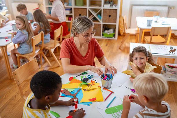 istock Preschool teacher assisting diverse children with arts and crafts using scissors, glue, and colorful paper in a bright, cheerful classroom 2229128672