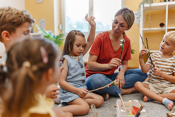istock Preschool teacher leading a fun interactive activity with children sitting in a circle, raising hands and smiling in a bright classroom 2229129445