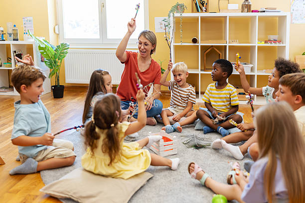 istock Preschool teacher leading a fun interactive activity with children sitting in a circle, raising hands and smiling in a bright classroom 2229129494