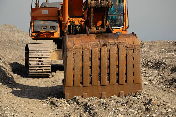 An orange excavator stands on a construction site. Its boom is outstretched and the bucket touches the ground. The heavy-duty machine is used for digging, excavation work. Front view, close-up