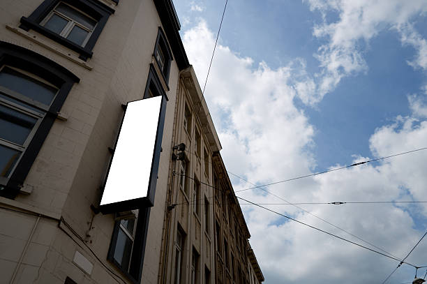 Empty billboard signage mockup hanging on a building facade with a cloudy sky background