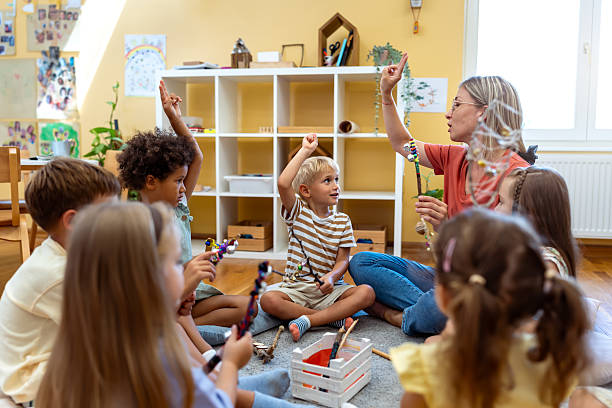 istock Preschool teacher leading a fun interactive activity with children sitting in a circle, raising hands and smiling in a bright classroom 2229138481