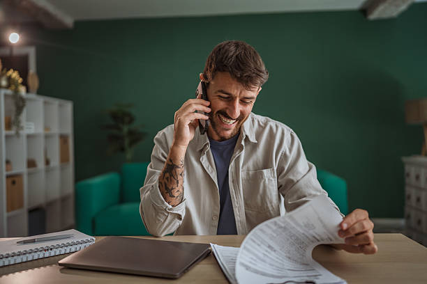 istock Happy entrepreneur talking on phone and reviewing documents at home office 2229140933