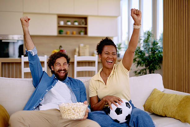 istock Excited couple cheering while watching soccer match at home 2229142577