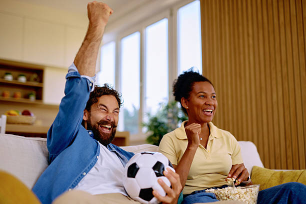 Excited couple cheering while watching soccer match at home