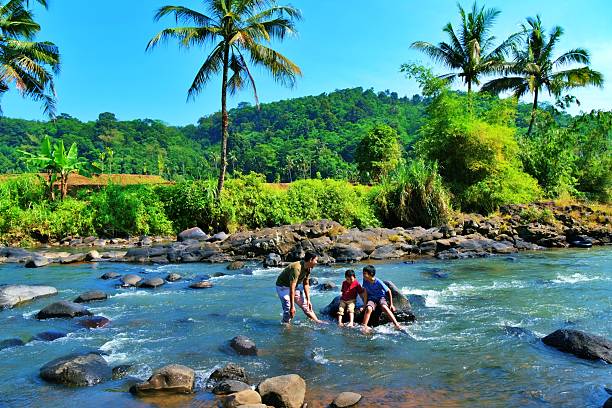 A man and his childrens standing on rocks and enjoying the summer river scene.