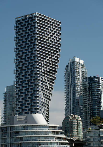 Looking at striking image of a uniquely designed skyscraper, leaning dramatically amongst more traditional high-rises from Granville Island.\nThe architectural contrast showcases modern urban development