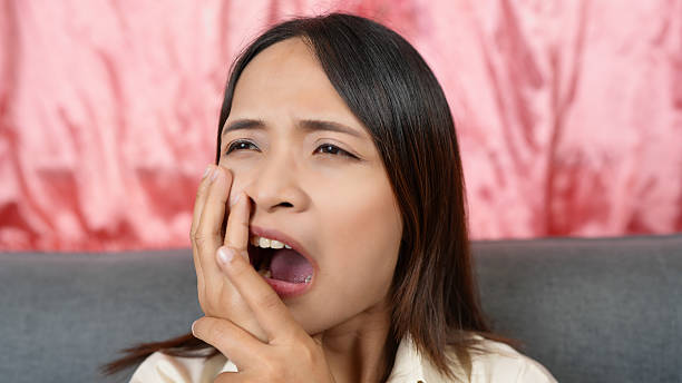 istock Woman expressing discomfort while holding her face, possibly indicating toothache or dental pain. background features soft, pink fabric, adding contrasting element to scene 2229174203