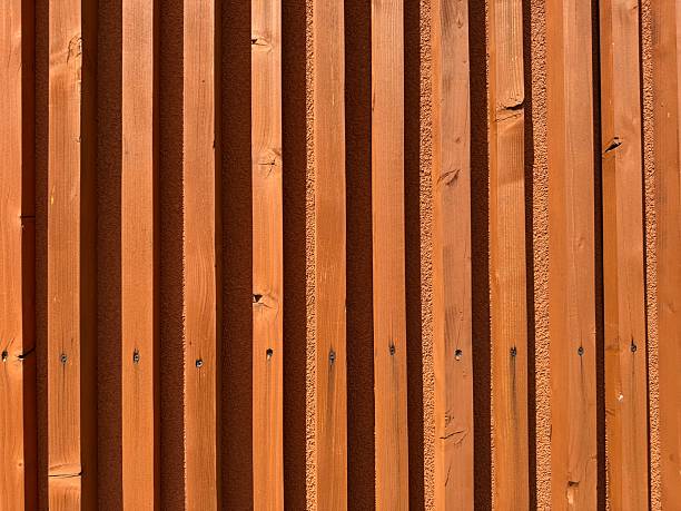 Terracotta colored wooden wall with strong vertical rhythm sunlight shadow contrast texture minimalist building facade background natural architecture earthy modern tones warm outdoor detail